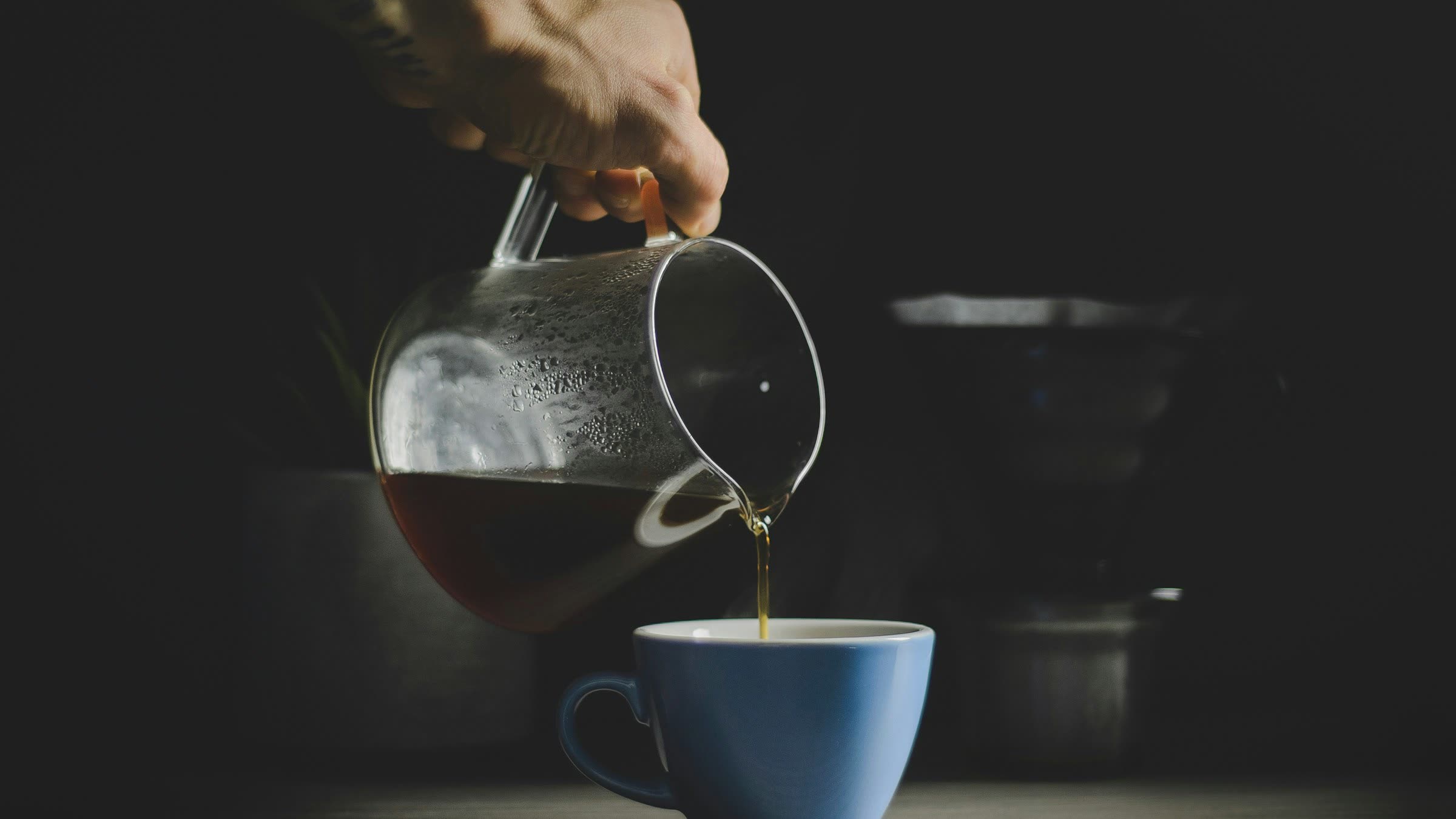 Single-origin coffee beans beside a slow pour-over, lit low against dark stone.